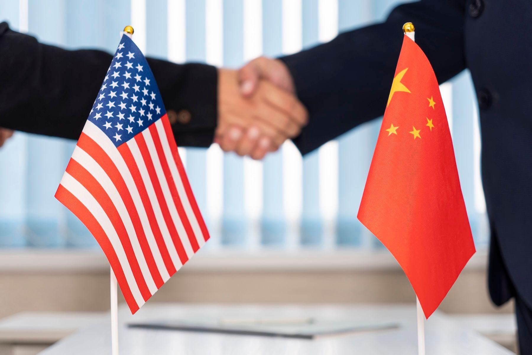 China USA Politik, China Politik, Wirtschaft, Sanktionen, Verhandlungen: Flaggen von China und den USA stehen auf einem Tisch, dahinter geben sich zwei Männer die Hand